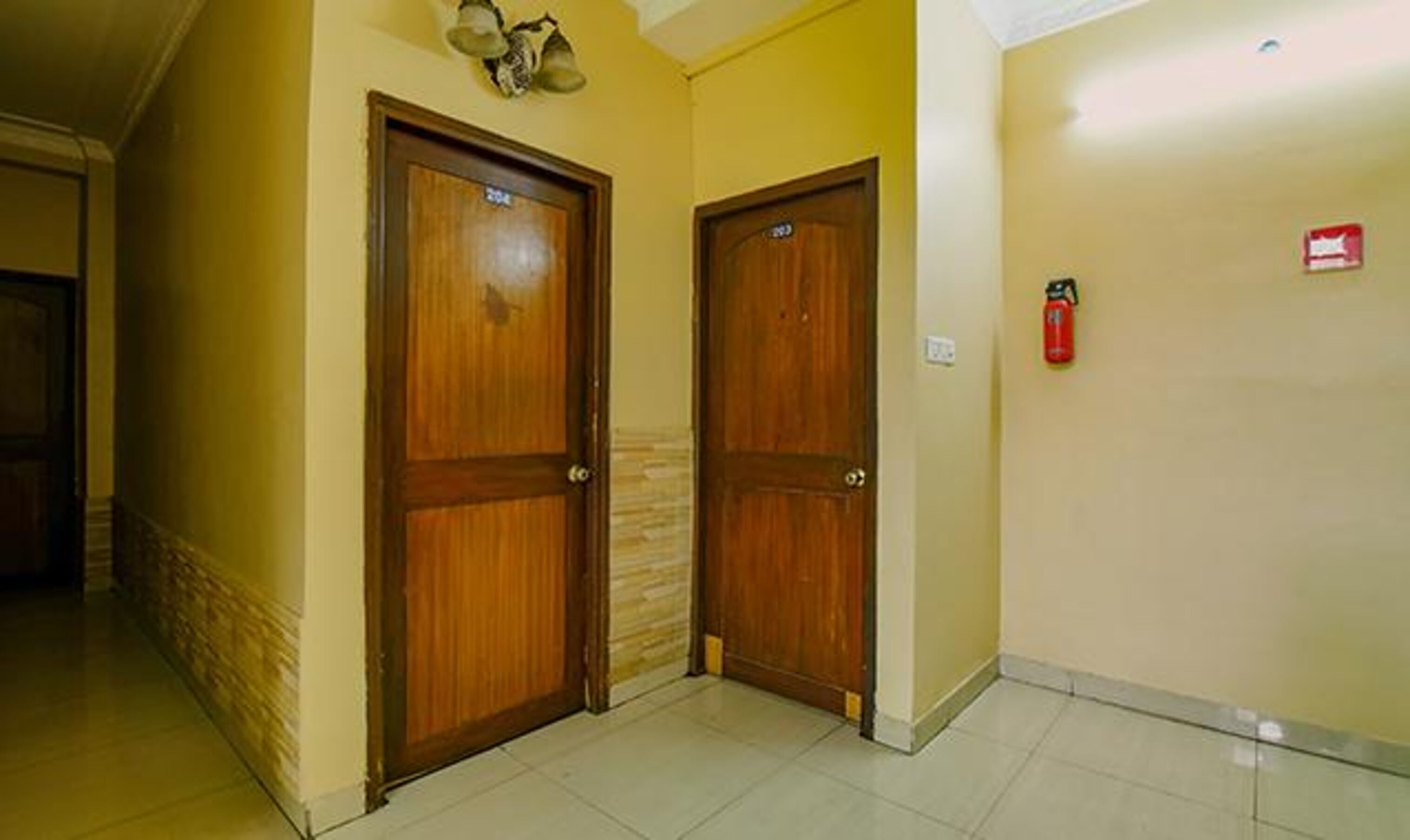 A hallway with two wooden doors, a fire extinguisher on the wall, and a tiled floor.