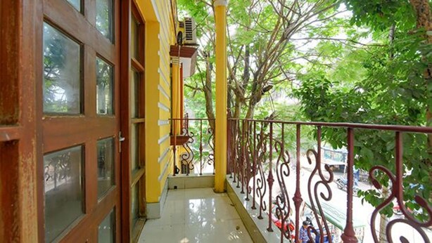 A balcony with a yellow railing, a wooden door, and a view of trees. - Fabexpress Elight Residency (Bidhannagar)