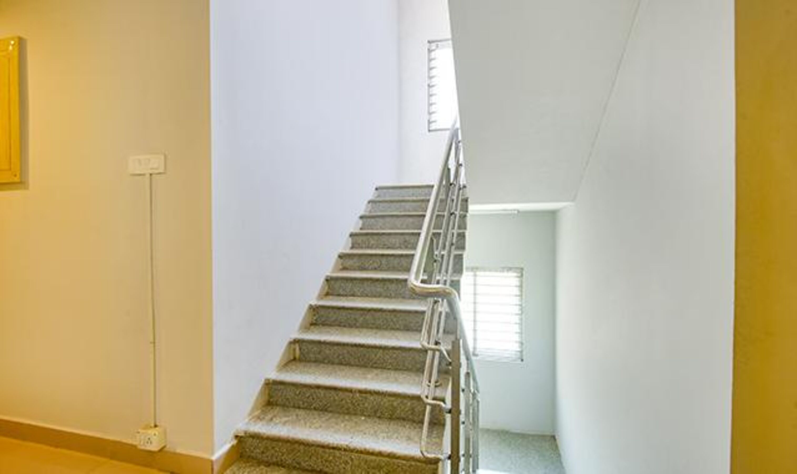 Una escalera con barandilla, escalones alfombrados y una pared lisa.