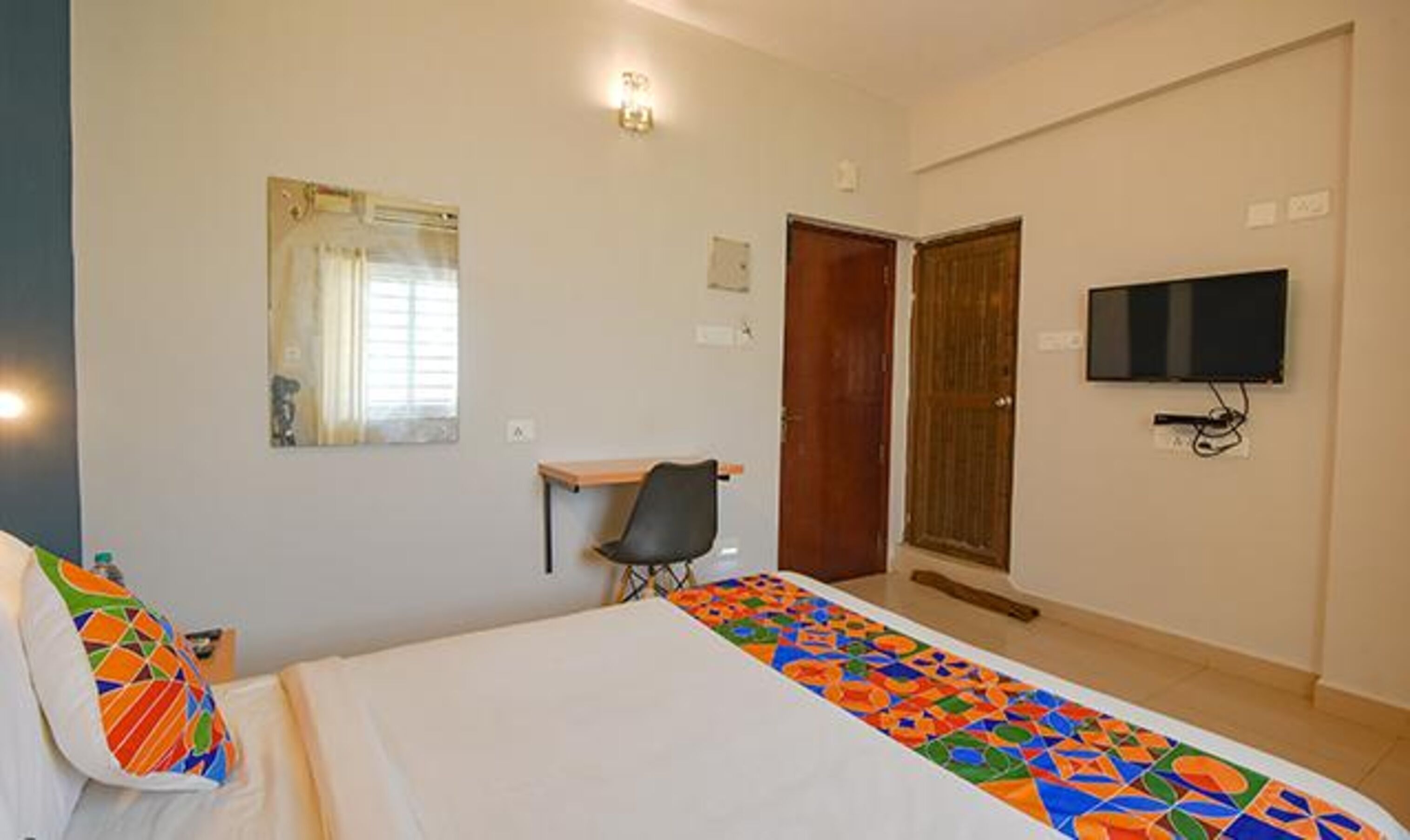 Une chambre d’hôtel avec un lit, un bureau, une chaise, une télévision et une porte.
