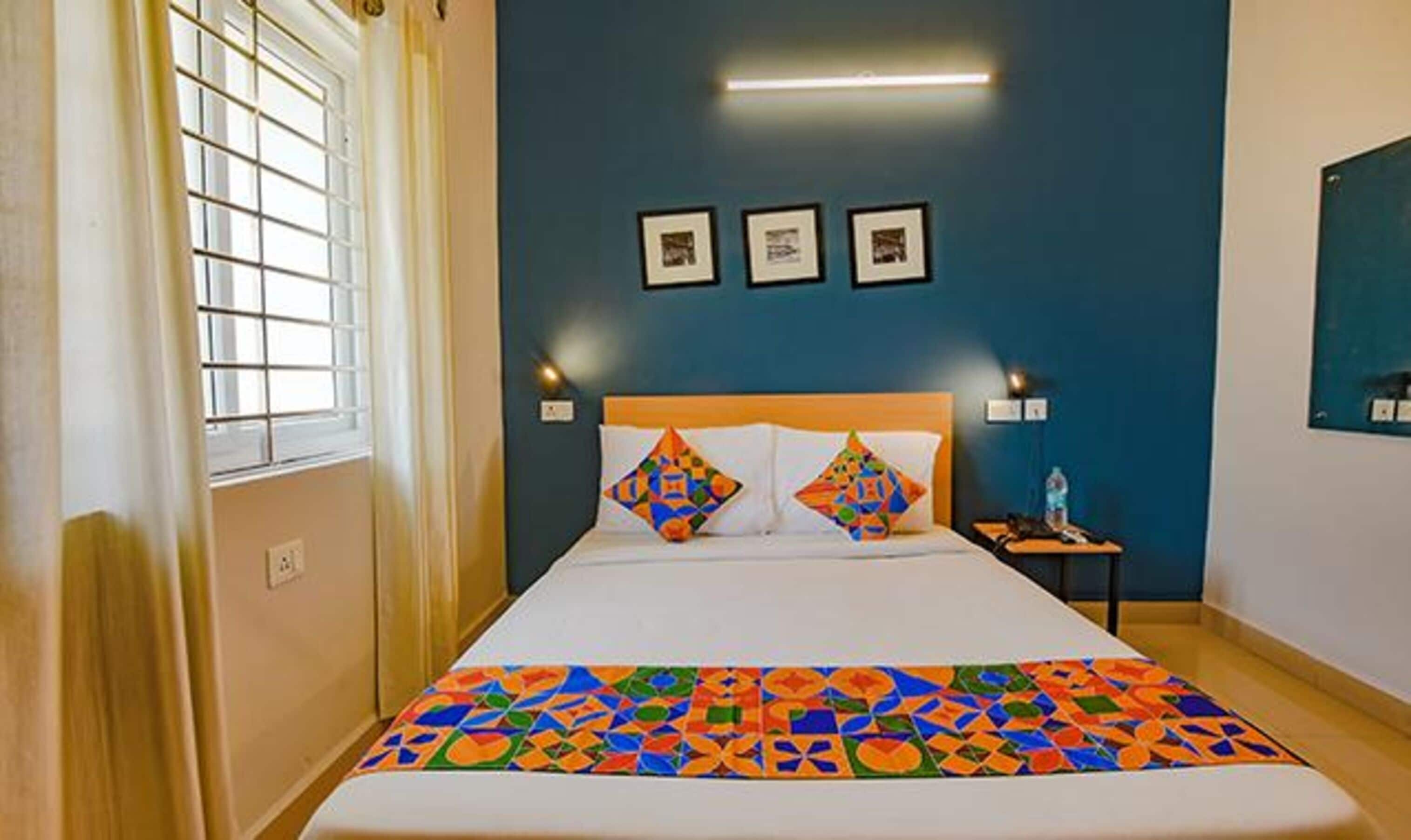 A hotel room with a bed, a nightstand, and a window with blinds.