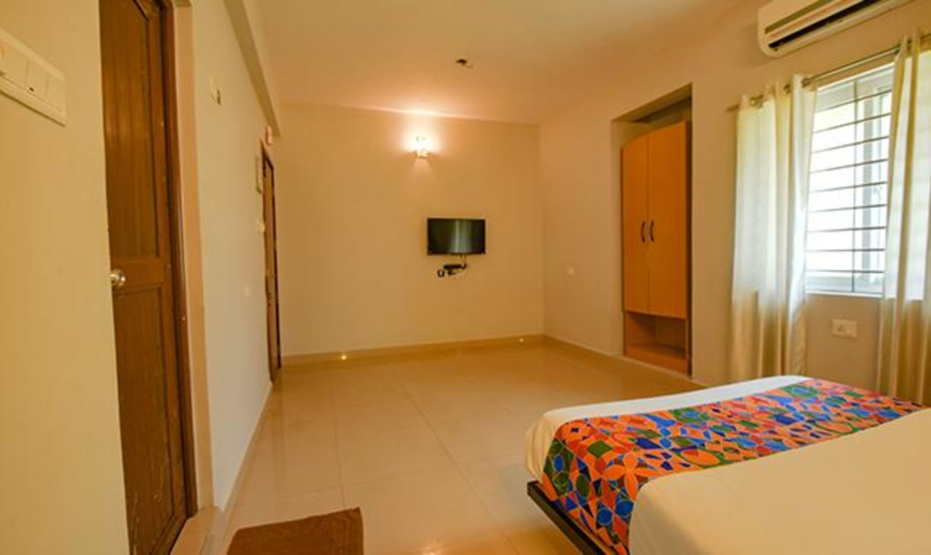 A hotel room with a bed, a television, a wardrobe, and a window with curtains.