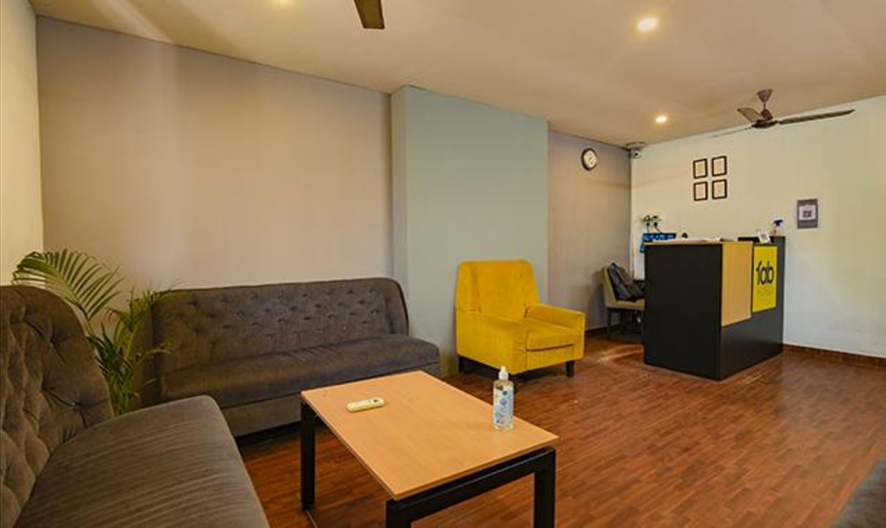 Una habitación con un sofá, un sillón amarillo, una mesita con un control remoto y un mostrador de recepción.