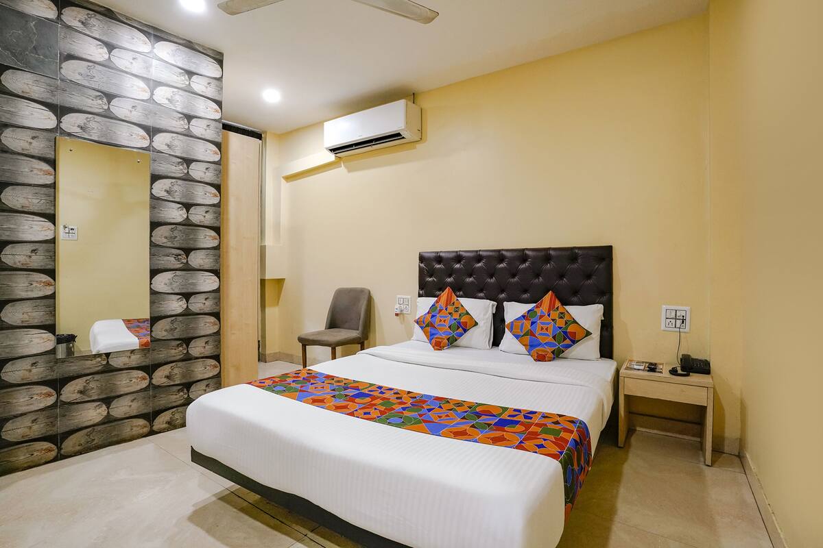 Habitación de hotel con una cama grande, cabecera, mesita de noche, una silla, un espejo y un equipo de aire acondicionado.