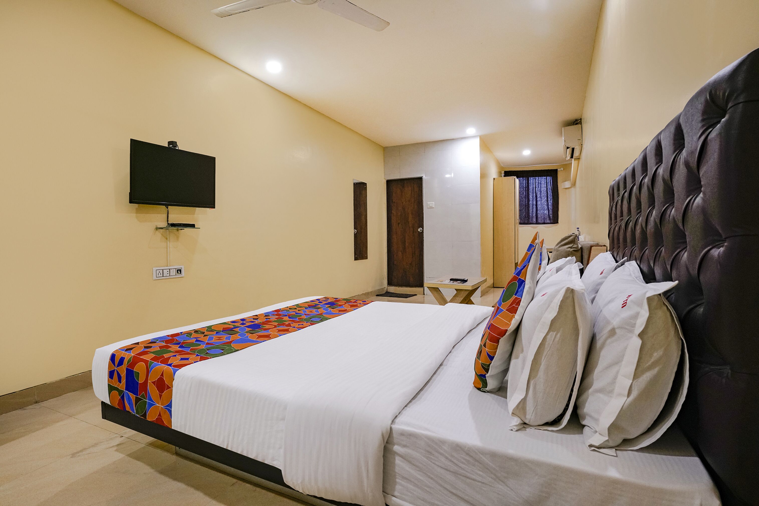 A hotel room with a bed, a television mounted on the wall, and a ceiling fan.
