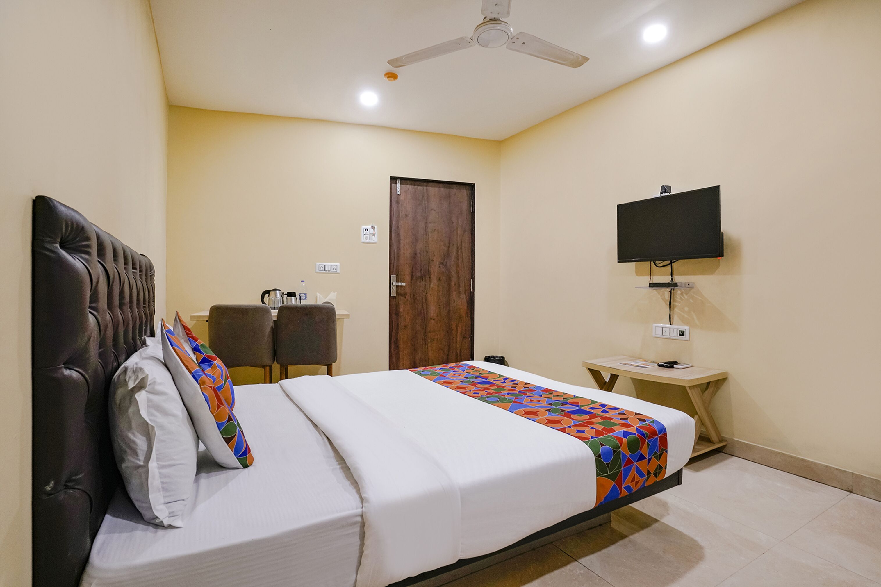 A hotel room with a bed, a desk, a chair, a television, and a ceiling fan.