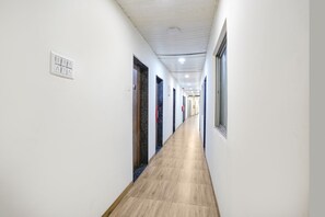Un long couloir étroit aux murs blancs, doté d’un plancher en bois et de portes donnant sur différentes pièces.