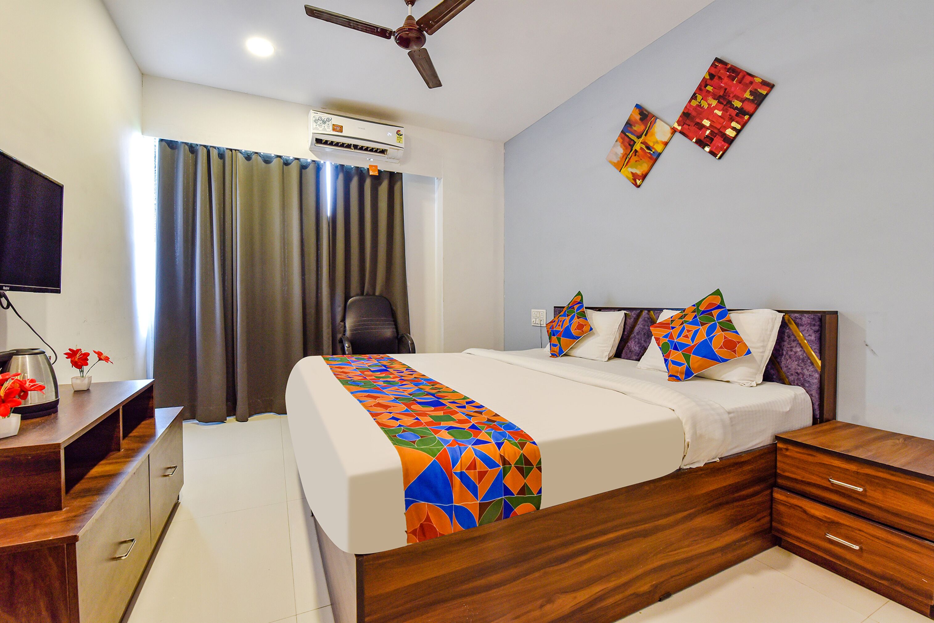 A hotel room with a bed, a desk, a chair, an air conditioner, and a ceiling fan.