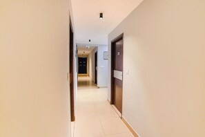 A hallway with a door on the right, a light fixture on the ceiling, and a door at the end. - Fabhotel Earth (Chennai)