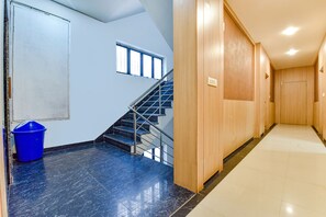 A modern hotel hallway with a blue-tiled floor, a wooden door, and a staircase with metal railings. - Fabhotel Alexa (Jaipur)