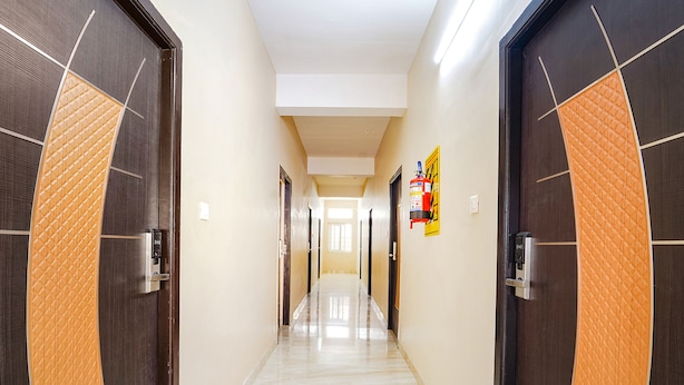 A hallway with dark wooden doors, a fire extinguisher on the wall, and a clean, tiled floor. - Fabexpress Uv Residency (Coimbatore)
