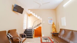 A waiting area with leather chairs, a television mounted on the wall, a staircase, and a statue. - Fabexpress Uv Residency (Coimbatore)