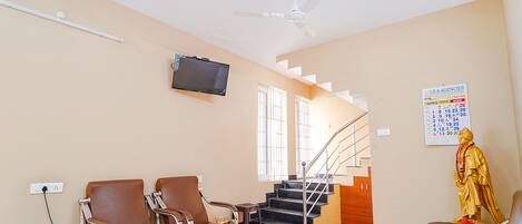 Un salon avec un téléviseur, deux fauteuils, une table basse, une statue et un escalier.