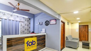 Un hall d'hôtel avec un comptoir d'accueil portant l'inscription « fab hotels », un ventilateur de plafond, un mur à motifs et un canapé gris.