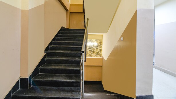 Un escalier avec des marches noires et une rampe métallique, menant à un palier doté d’un mur orné de motifs et d’un luminaire.