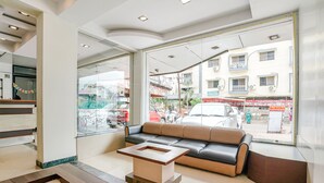 A modern lobby with a leather sofa, a wooden coffee table, and large windows offering a view of the street outside. - Fabhotel Kingdom Sai (Rahata)