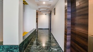A hallway with a marble floor, a sign indicating the second floor, and a wooden door on the right. - Fabhotel Kingdom Sai (Rahata)