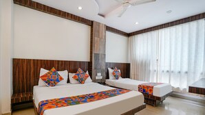 A hotel room with two beds, a wooden headboard, a large window with curtains, and a ceiling fan. - Fabhotel Kingdom Sai (Rahata)