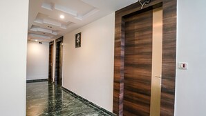A modern hallway with polished marble floors, wooden doors, recessed lighting, and a plain wall with a single artwork. - Fabhotel Kingdom Sai (Rahata)