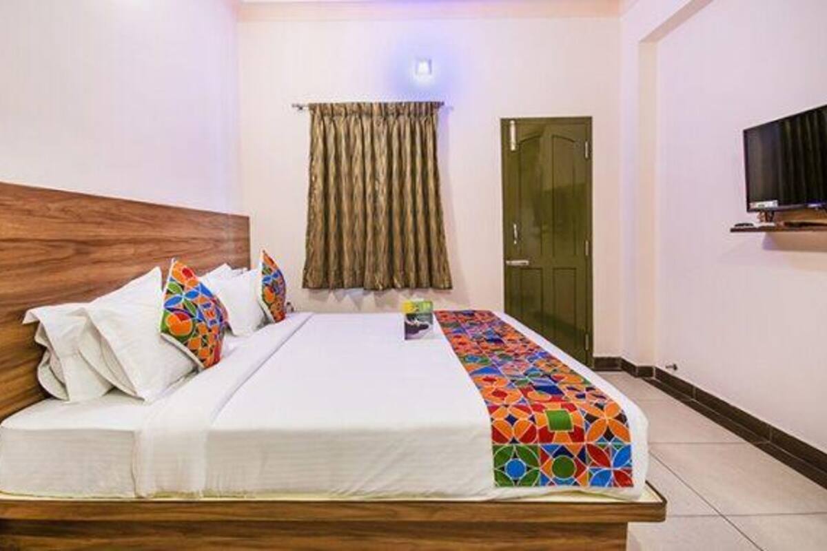 A neatly made bed with a wooden headboard, a colorful throw blanket, and a single pillow.