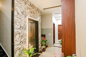 A hallway with a marble wall, an elevator, and potted plants. - FabHotel Golden City (Amritsar)