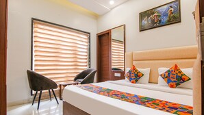 A hotel room with a bed, a chair, a window with blinds, and a painting on the wall. - FabHotel Golden City (Amritsar)