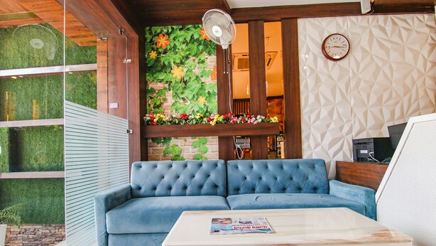 A modern living room with a blue sectional sofa, a white coffee table, and a wall-mounted fan. - FabHotel Golden City (Amritsar)