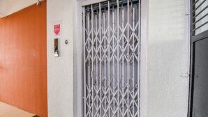 Pared blanca con una reja metálica, un letrero de ascensor y una zona de césped artificial verde.