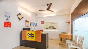 Zona de recepción de un hotel, con mostrador de recepción, televisión, ventilador de techo y un cartel dando la bienvenida a los huéspedes.