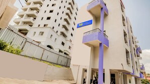 Un edificio de varios pisos con un letrero que dice 'Fab Hotels'. Cuenta con balcones, fachada de concreto y un estacionamiento con una moto.