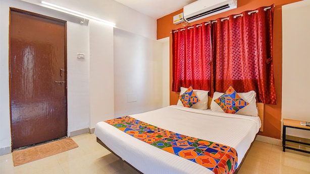 Habitación de hotel con cama, puerta, equipo de aire acondicionado y ventana con cortinas rojas.