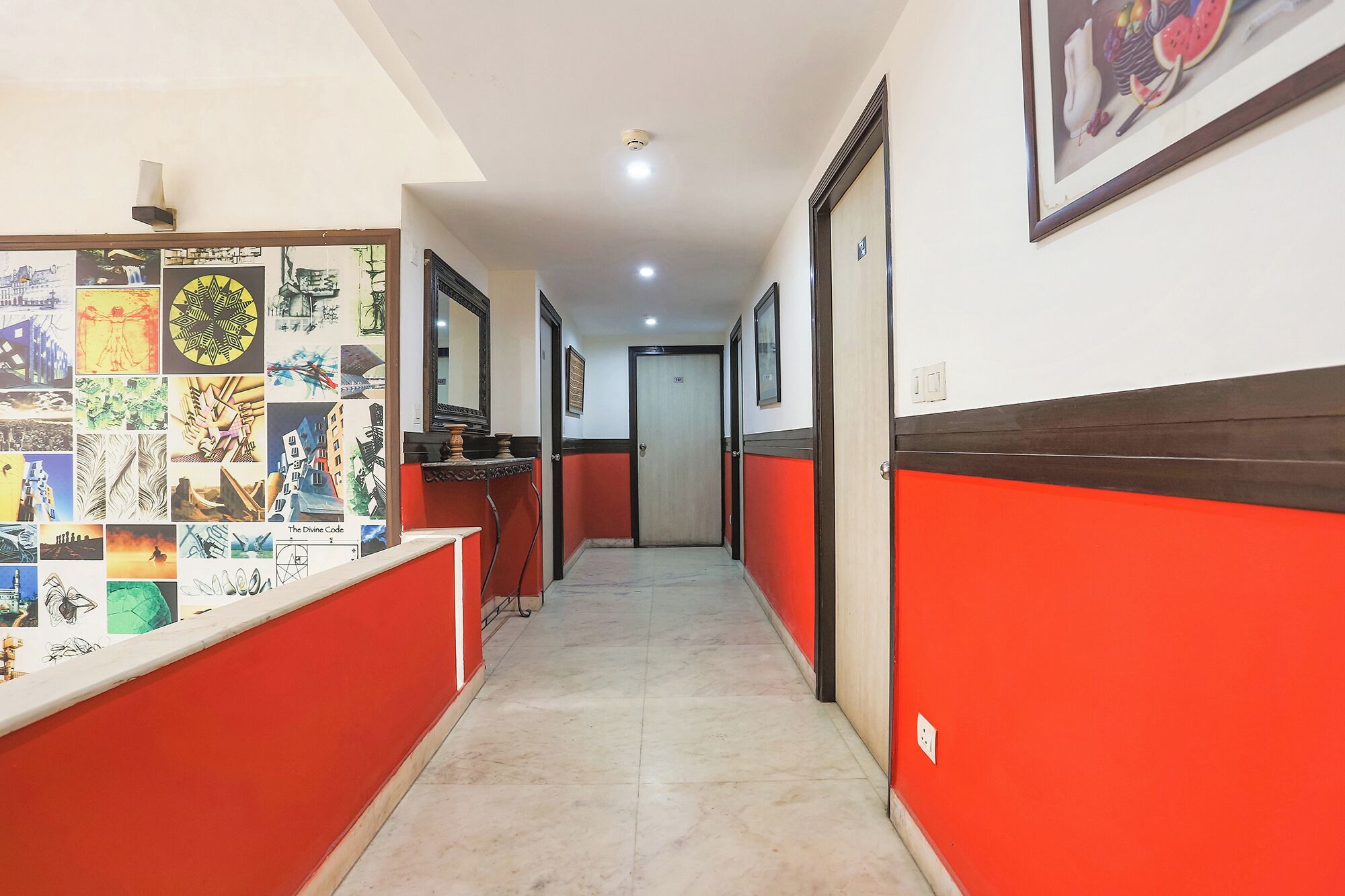 A hallway with red and white walls, a tiled floor, and a series of framed pictures on the left wall.