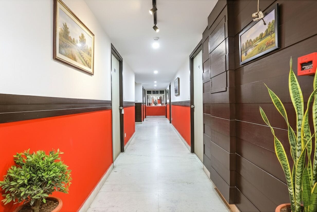 A hotel corridor with red and white walls, a tiled floor, and framed pictures on the walls.