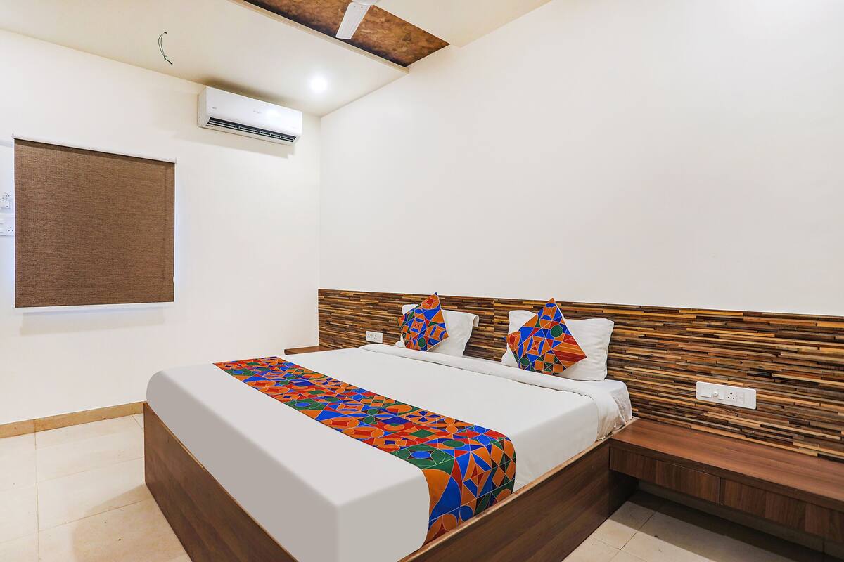 Uma cama bem arrumada com um edredom colorido de padrão geométrico, uma cabeceira de madeira e uma mesa de cabeceira com abajur.