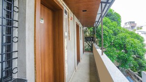 A narrow corridor with wooden doors and a metal gate, leading to a balcony with a view of greenery and buildings. - Fabexpress Jai Manglam Service Apartment (Nagpur)