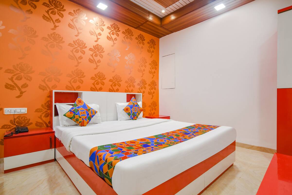 Une chambre moderne avec un grand lit, un papier peint à motifs floraux orange et un mur d’accent rouge.