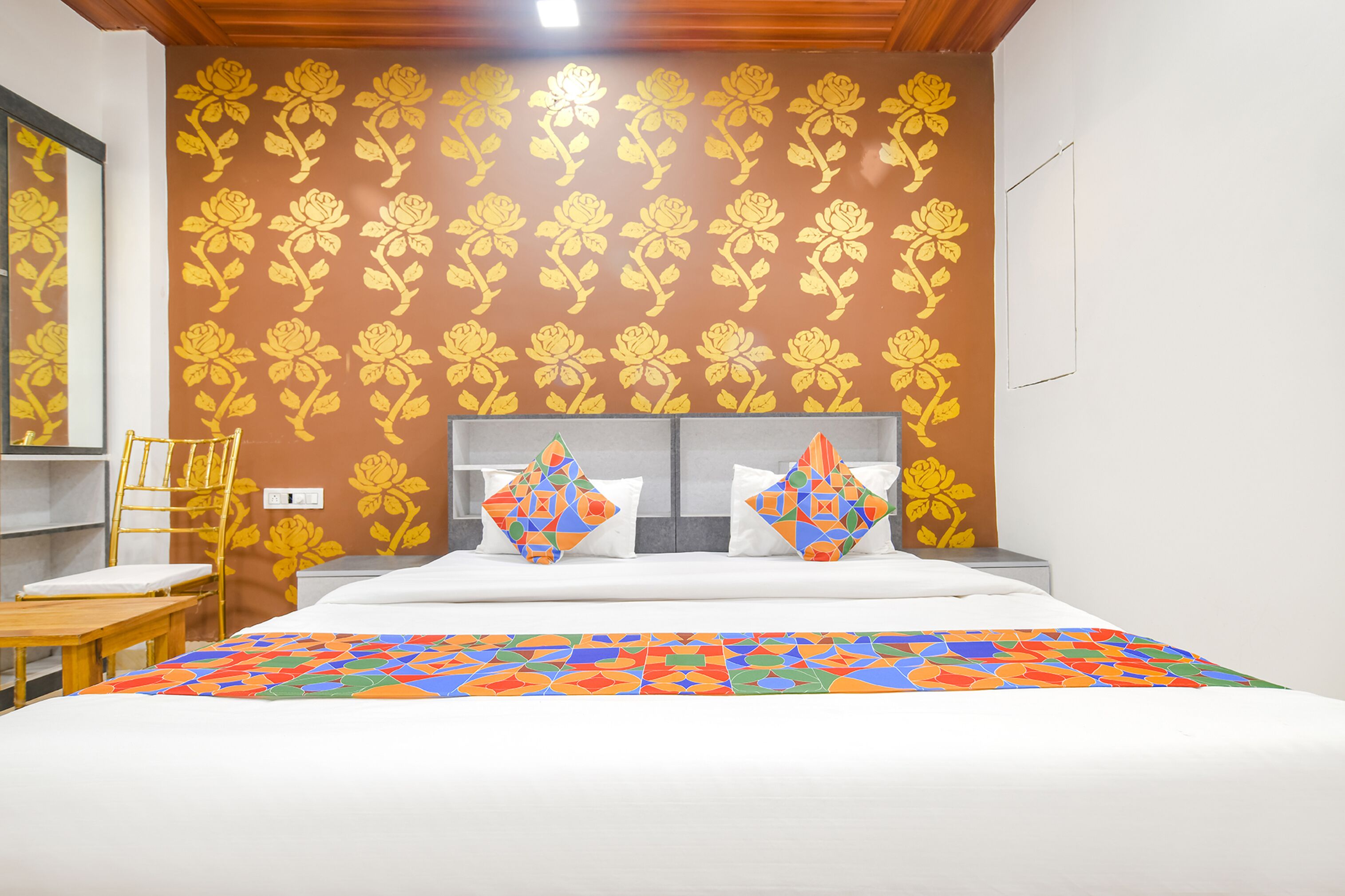 Une chambre d’hôtel avec un lit, une tête de lit en bois, une courtepointe aux couleurs vives et un mur orné d’un motif floral.
