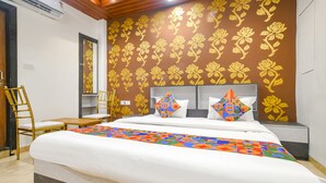 A hotel room with a large bed, two pillows, a wooden chair, and a wall with a floral pattern. - FabHotel Dream Paradise (Indore)