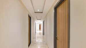 Um corredor comprido e estreito com piso de mármore polido, portas de madeira e iluminação embutida.