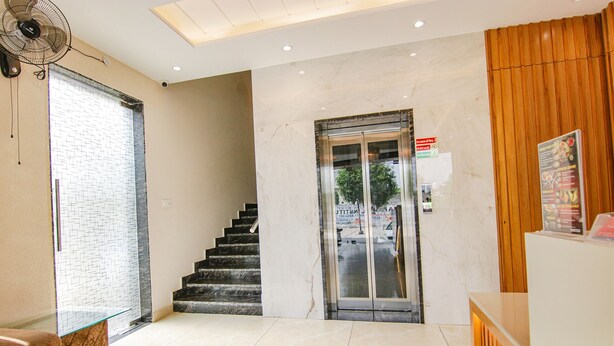 Um hall de hotel com balcão de recepção, escada e elevador de vidro.