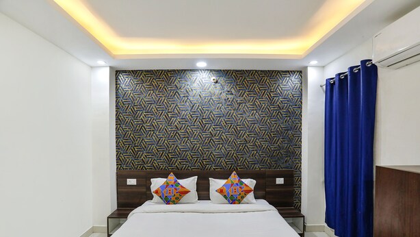 A hotel room with a patterned wallpaper, a bed with colorful pillows, and a blue curtain.
