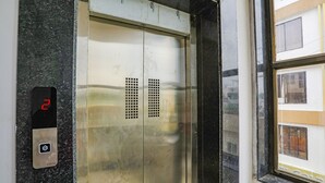 An elevator with a digital display showing the number 2, a metallic interior, and a window with reflections of buildings.