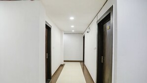 A narrow hallway with white walls, a tiled floor, and dark wooden doors.