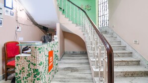 A staircase with a marble finish, a reception desk with a green leafy pattern, and a red chair. - Fabexpress Karunamoyee Regency (Barasat)