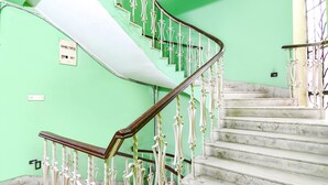 A staircase with white balusters and a wooden handrail, leading to a landing with a green wall and a white ceiling. - Fabexpress Karunamoyee Regency (Barasat)