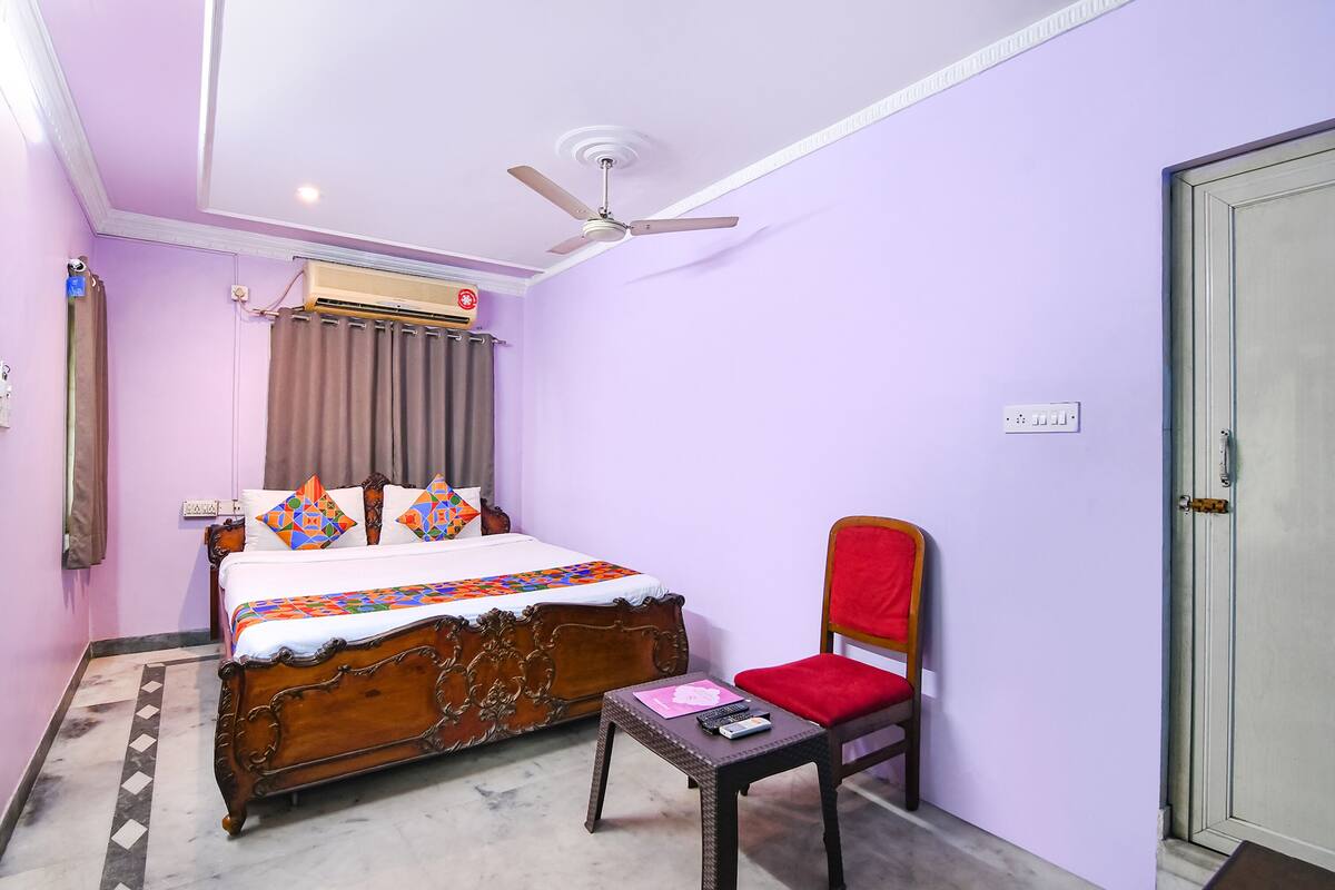 A bedroom with a wooden bed, a red chair, a ceiling fan, and an air conditioning unit.