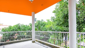 A covered outdoor area with white columns and a white railing, overlooking a green park with trees and a building in the background. - Fabexpress Karunamoyee Regency (Barasat)