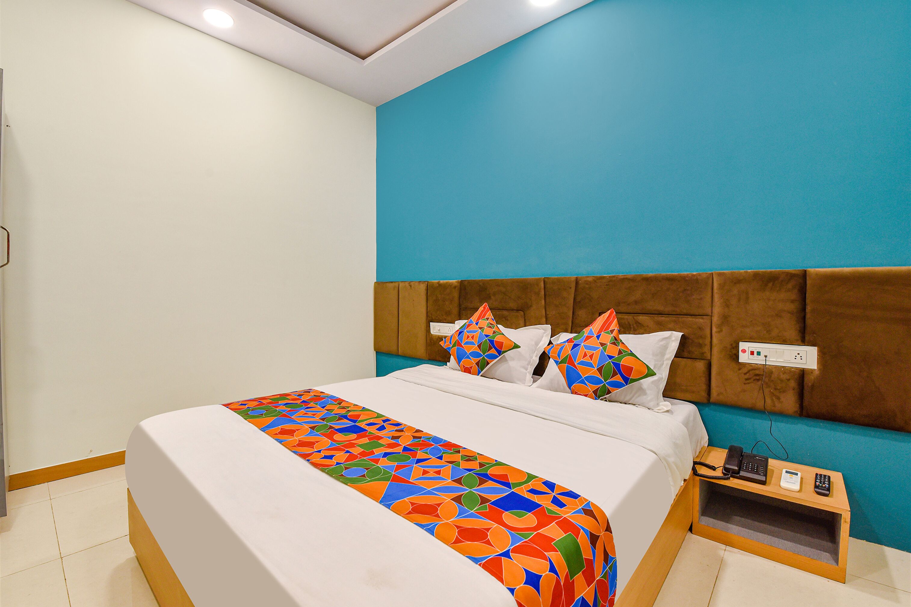 Een hotelkamer met een bed, nachtkastje en een stopcontact aan de muur.