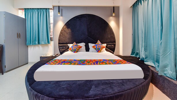 A modern bedroom with a large bed, a curved headboard, and teal curtains. - Fabhotel Sky Palace (Surat)