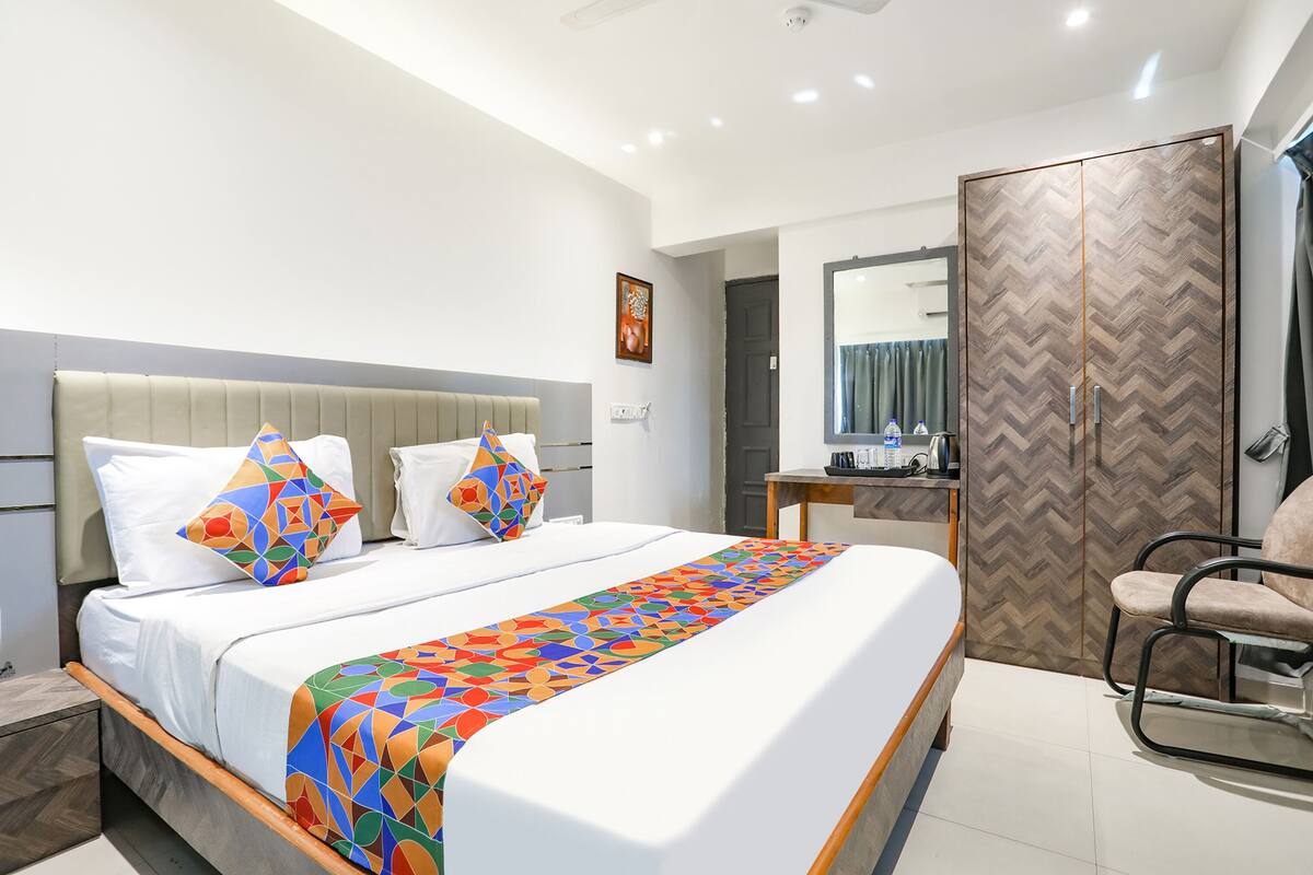 A modern hotel room with a large bed, a desk, a wardrobe, and a chair.